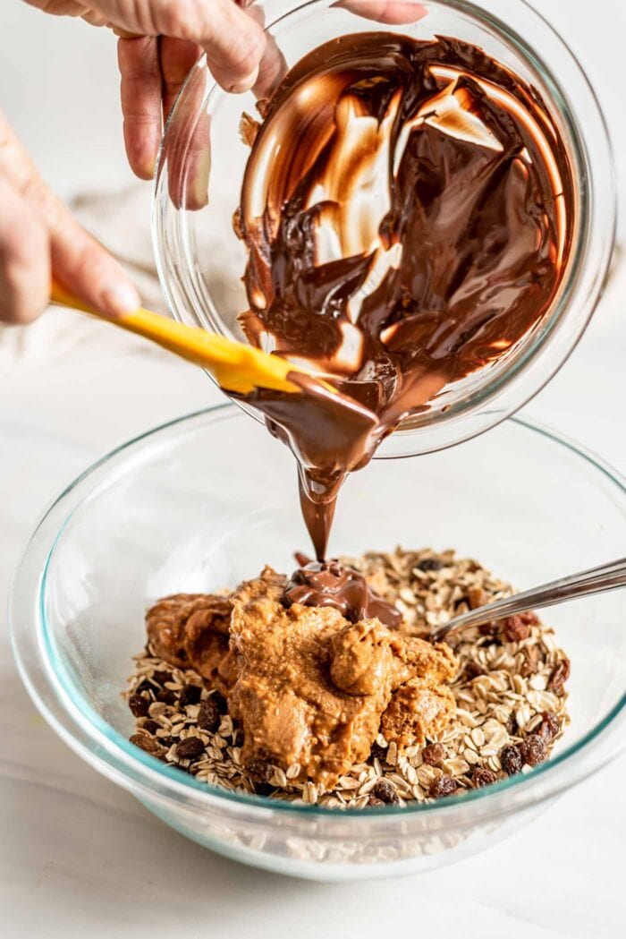 Pouring melted chocolate into a bowl of oats and peanut butter.