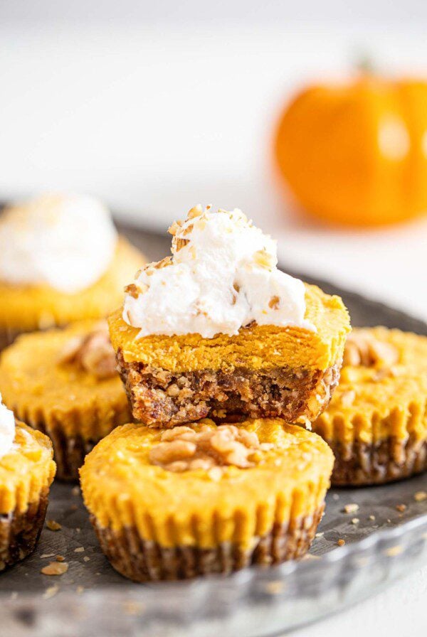 Front view of a pumpkin pie tart with a bit taken of it to show inside. Whipped cream on top.