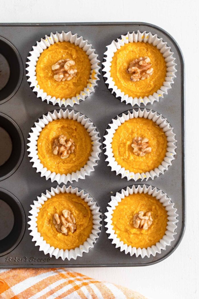 Overhead view of 6 pumpkin tarts topped with a few walnuts in cupcake liners in a muffin tin.