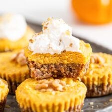 Front view of a pumpkin pie tart with a bit taken of it to show inside. Whipped cream on top.