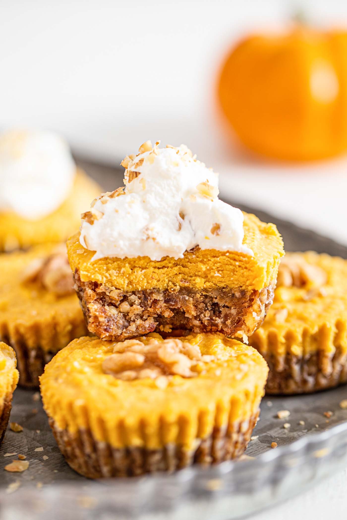 Front view of a pumpkin pie tart with a bit taken of it to show inside. Whipped cream on top.