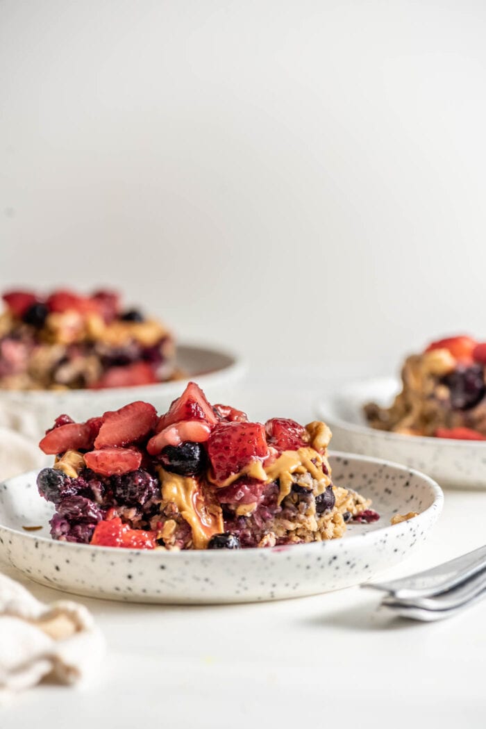 Baked oatmeal topped with berries on a plate with a spoon, two additional plates in background.