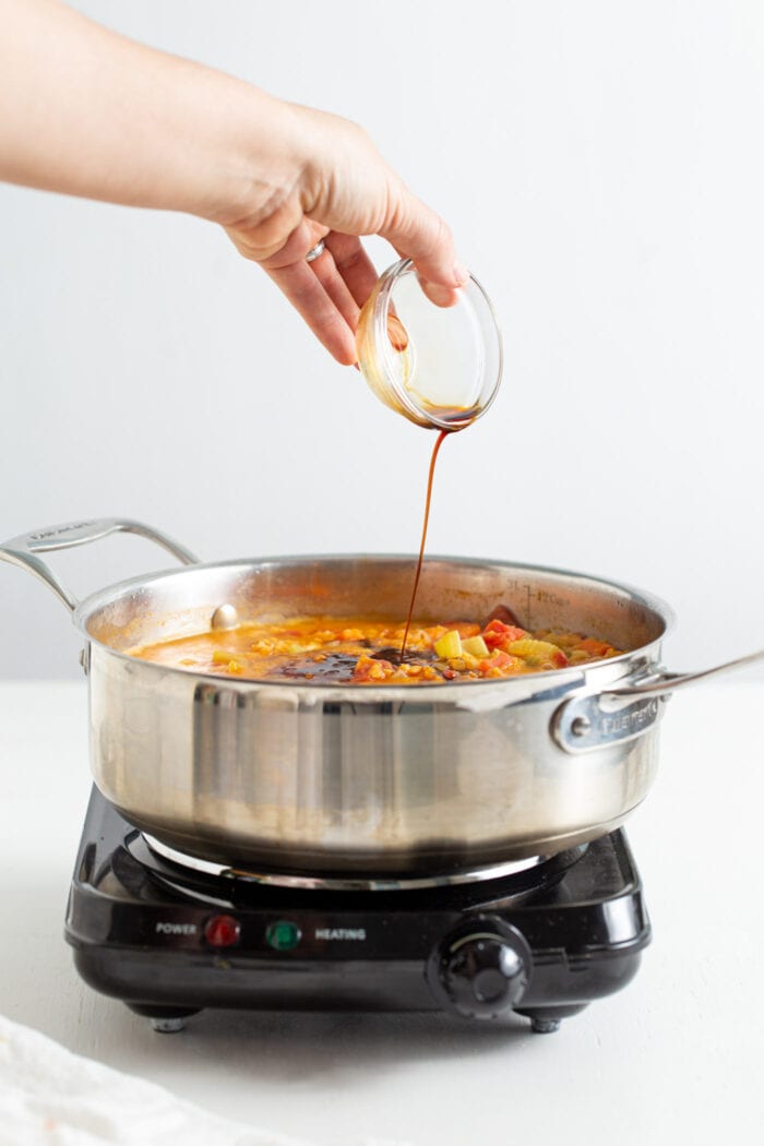 Pouring a small dish of soy sauce into a pot of soup.