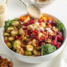 Drizzling a spoon of sauce over a salad with roasted vegetables and kale.