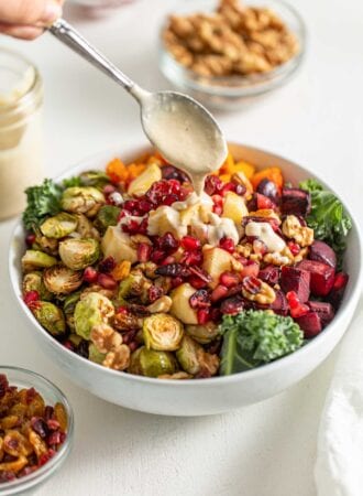 Drizzling a spoon of sauce over a salad with roasted vegetables and kale.