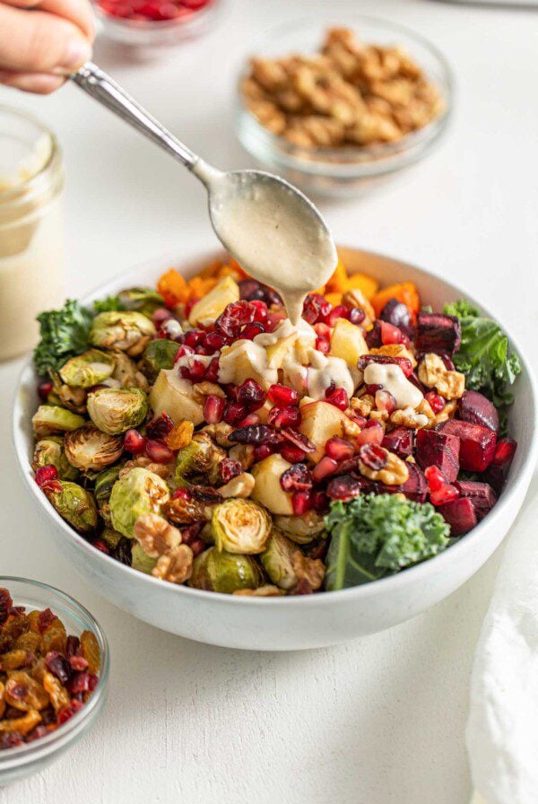 Drizzling a spoon of sauce over a salad with roasted vegetables and kale.