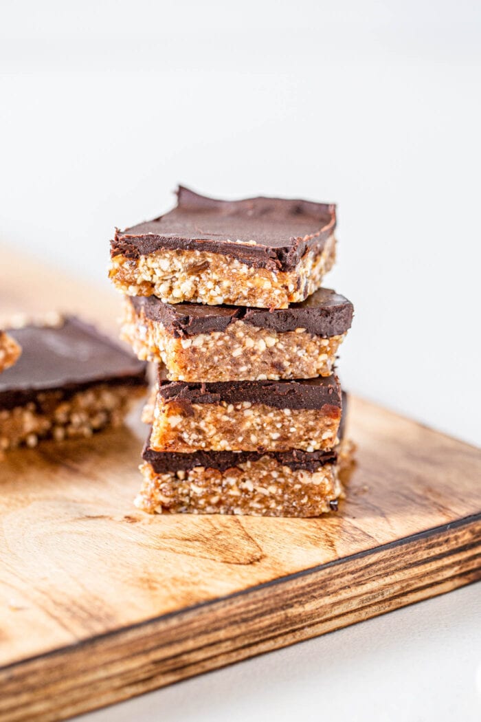 Stack of 4 chocolate coated cashew bars on a cutting board. More bars in background.