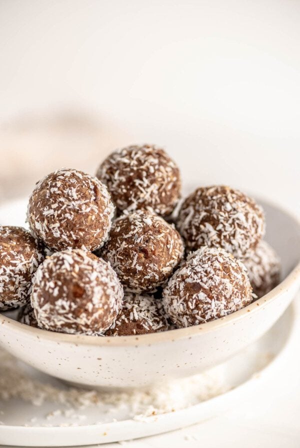 Bowl of protein balls rolled in coconut. Bowl sits on a plate.