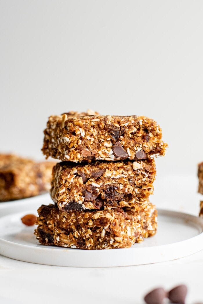 A stack of 3 no-bake oatmeal raisin bars with chocolate chips in them on a plate.