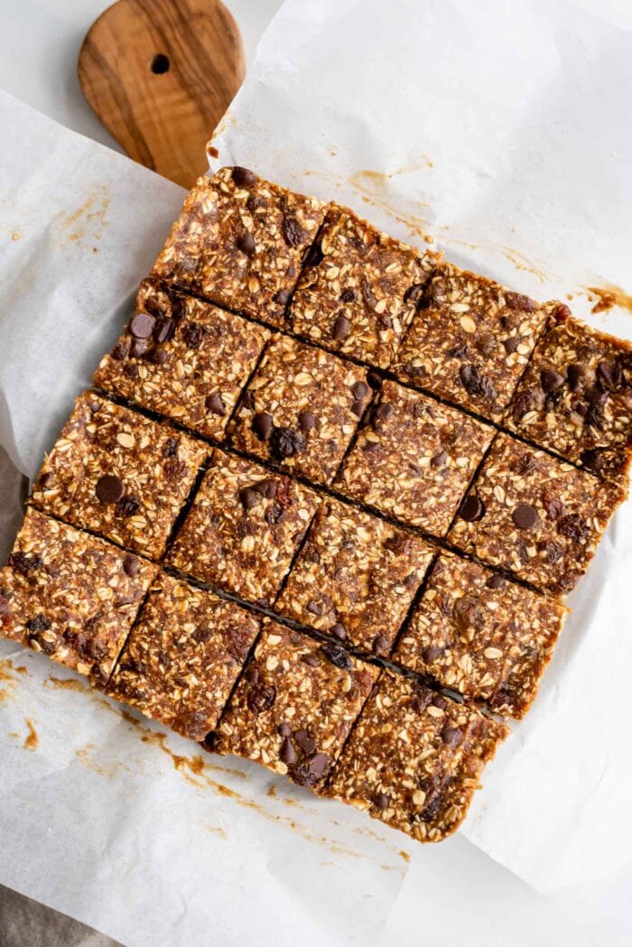 A batch of no-bake oatmeal raisin bars sliced into 16 square portions on a cutting board.
