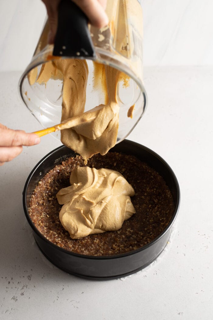 Scooping a creamy mixture from a blender into a crust in a springform pan.