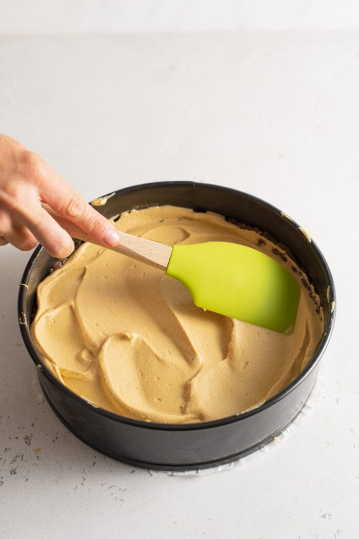 Using a spatula to spread a cheesecake filling into a springform pan.