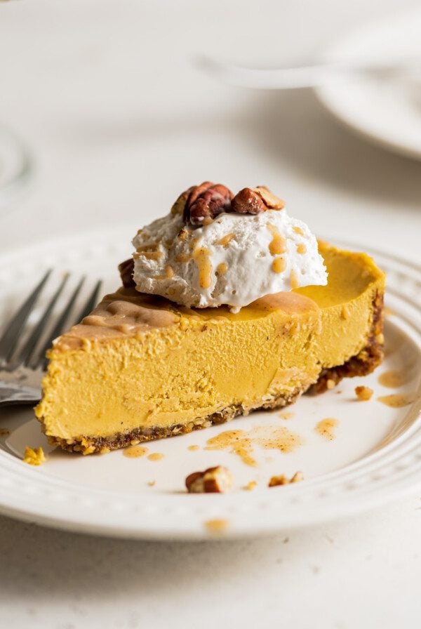 Slice of pumpkin cheesecake topped with whipped cream on a small plate. Fork rests on plate.