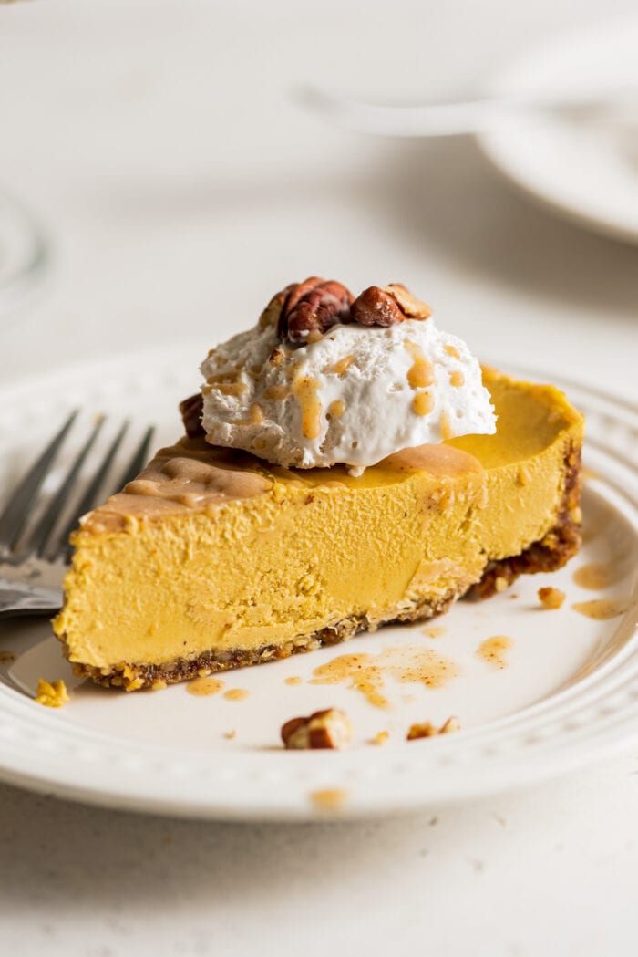 Slice of pumpkin cheesecake topped with whipped cream on a small plate. Fork rests on plate.