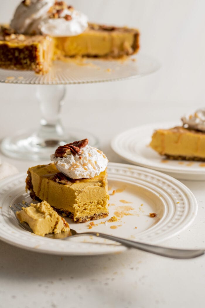 Slice of pumpkin cheesecake on a plate. Cake stand in background with rest of cake on it.