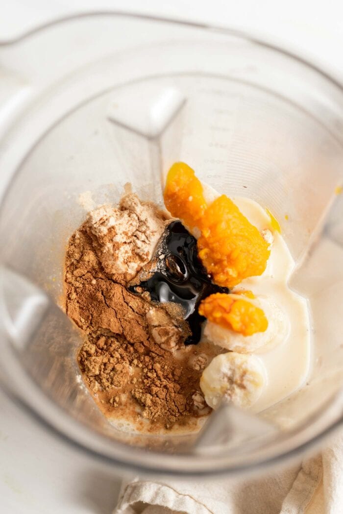 Pumpkin, frozen banana, milk and protein powder in a blender container.