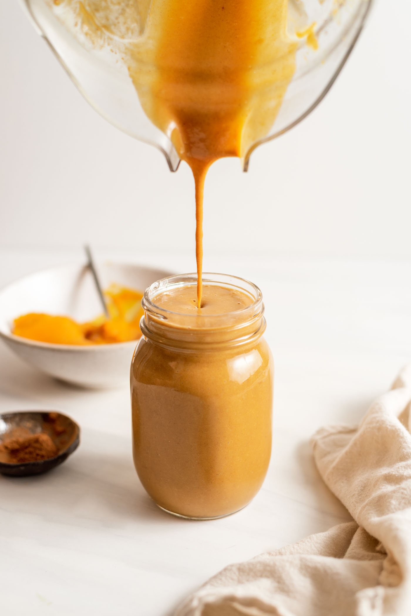 Blender pouring a pumpkin smoothie into a glass jar.