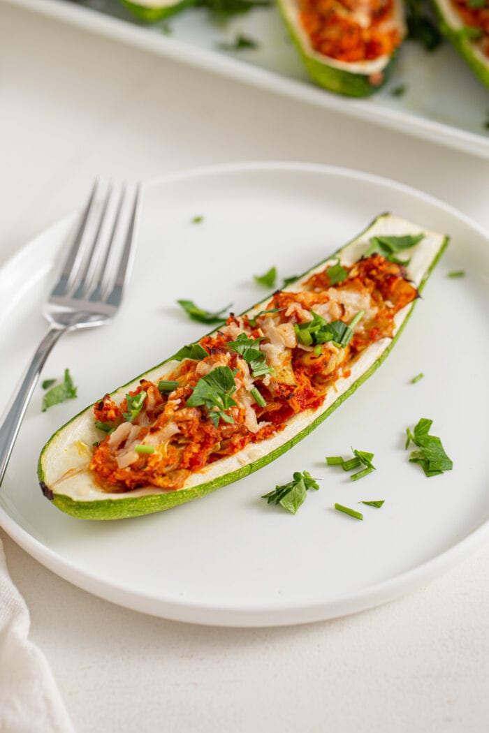 Half a zucchini on a plate stuffed with an artichoke and marinara sauce mixture. Fork rests on plate.