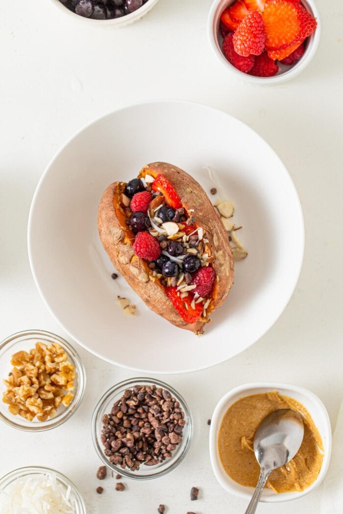 Overhead view of a baked sweet potato topped in a bowl with berries, peanut butter and almonds.