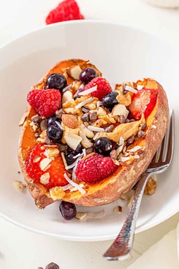 Close up of a baked sweet potato in a bowl topped with berries, almonds, peanut butter and coconut.