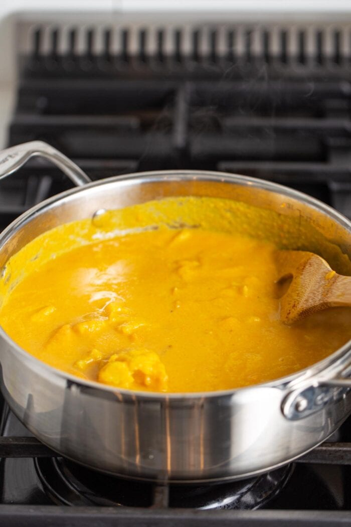 Pot of creamy sweet potato soup cooking on gas range stove. Wooden spoon rests in pot.