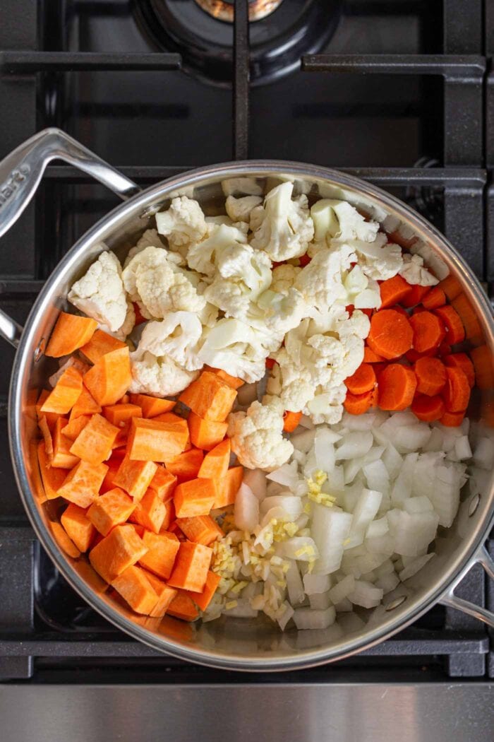 Sweet potato, cauliflower, carrot and onion cooking in a stock pot on a gas range stovetop.