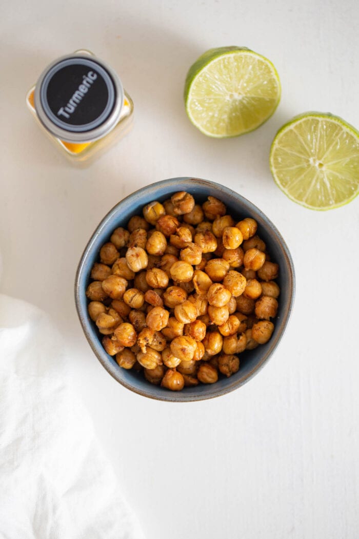 Overhead view of a bowl or roasted chickpeas. Cut open lime beside it.