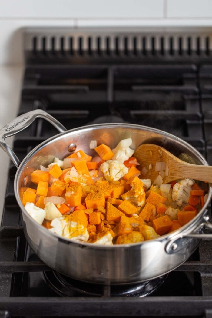 Sweet potato, cauliflower, carrot, onion and turmeric cooking in a stock pot on a gas range stovetop.