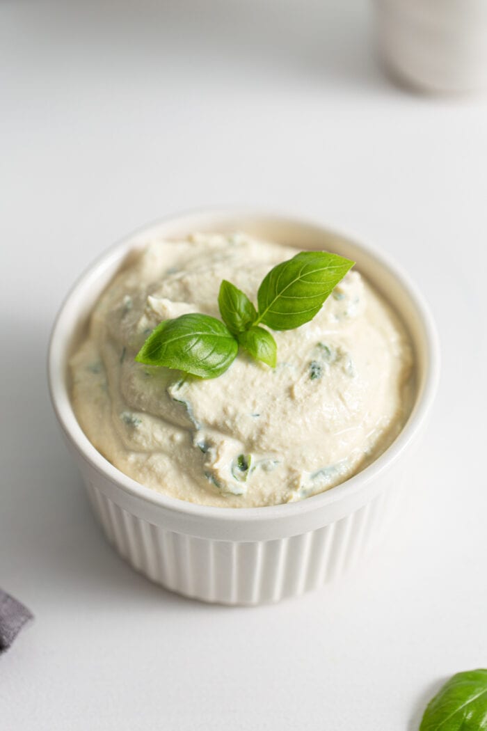 Small dish of herb ricotta topped with a piece of fresh basil.