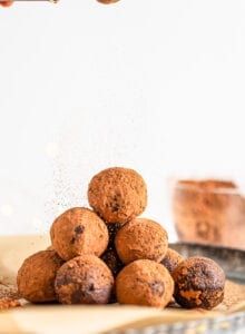 Stack of chocolate truffles on a plate being dusted with a sprinkling of cocoa powder.