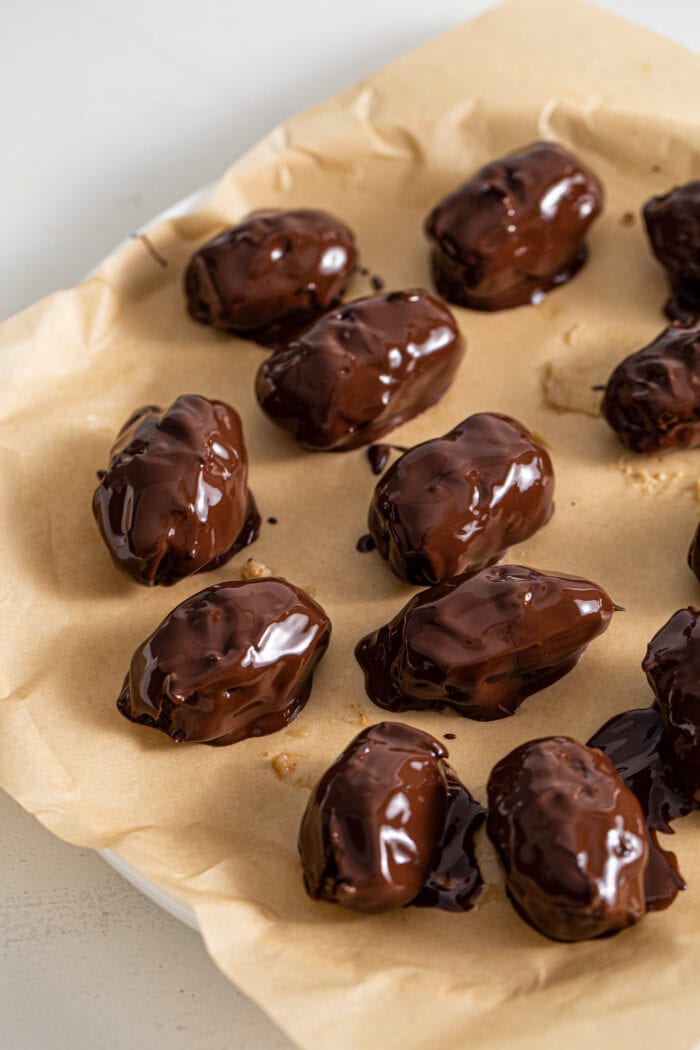 Chocolate covered dates on a parchment paper-lined plate.