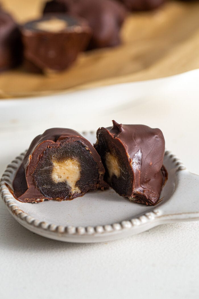 Cut open chocolate-covered medjool date with a peanut butter filling on a small plate.