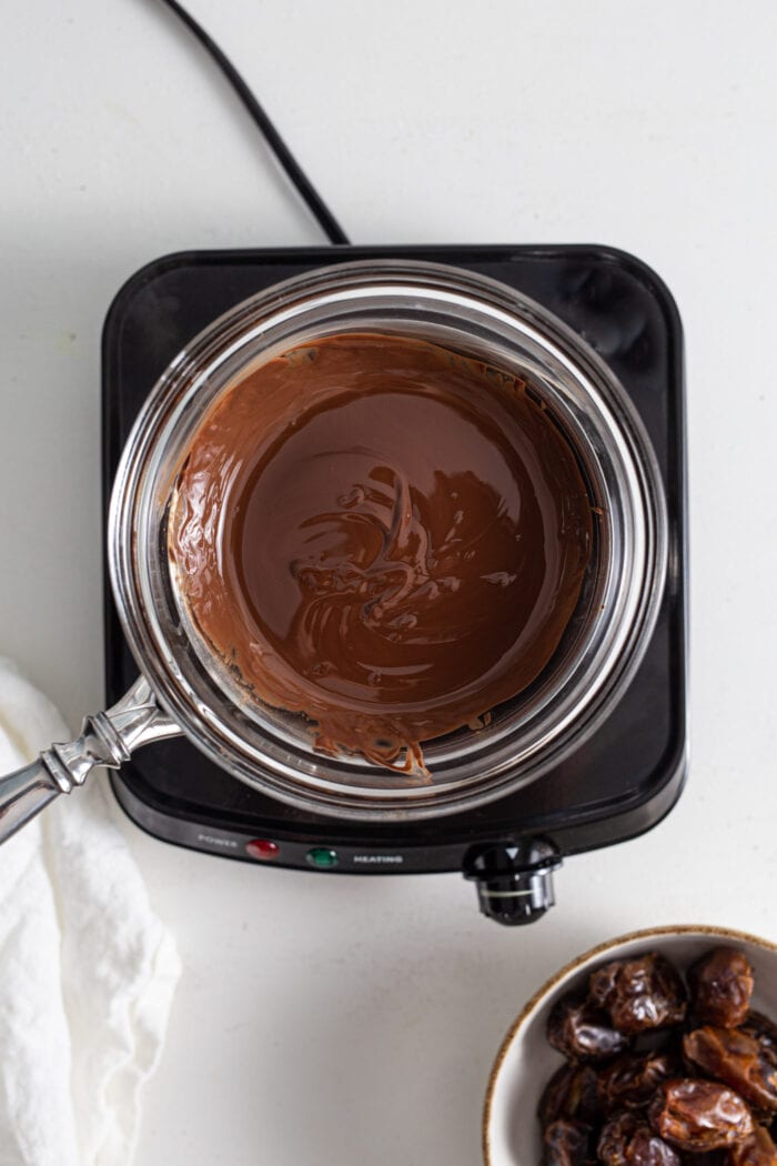 Melted chocolate in a double boiler on a small cooktop.
