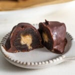 Cut open chocolate-covered medjool date with a peanut butter filling on a small plate.