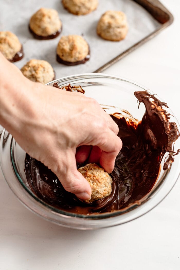 Hand dipping a coconut macaroon into a bowl of melted chocolate.