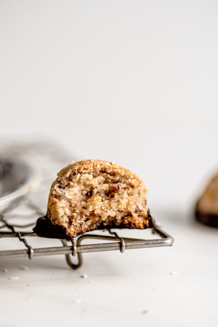 A chocolate-dipped coconut macaroon with a bite taken out of it sitting on a cooling rack.