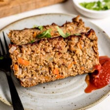 Two slices of vegetarian chickpea meatloaf on a plate with ketchup. Fork rests on plate.