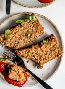 Two slices of vegan chickpea meatloaf on small plate with ketchup. Fork rests on plate.