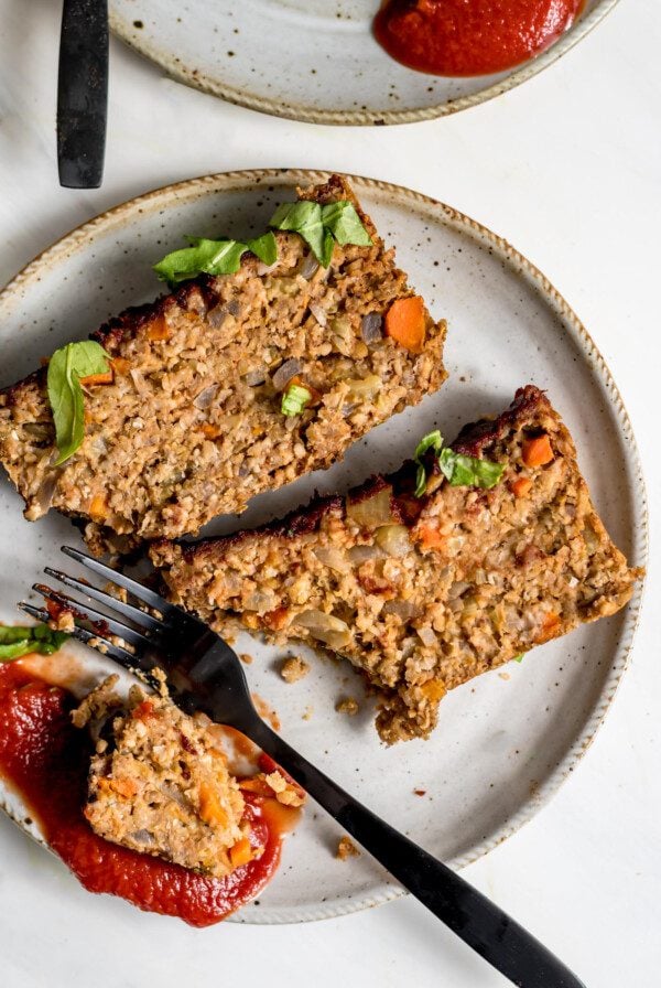 Two slices of vegan chickpea meatloaf on small plate with ketchup. Fork rests on plate.