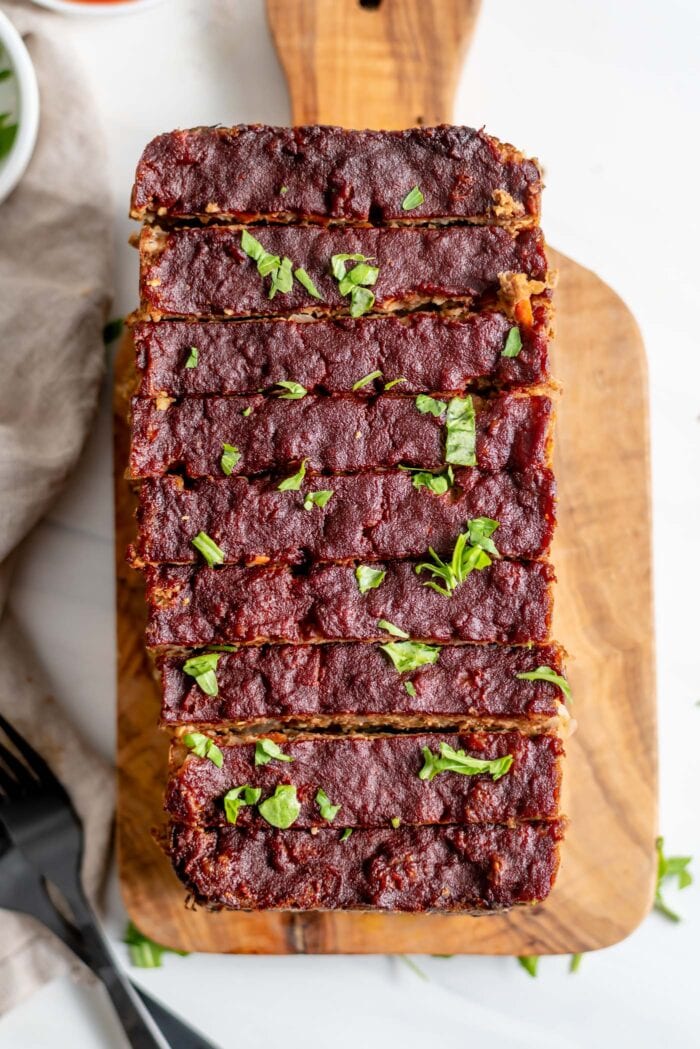 Overhead view of a vegetarian meatloaf cut into slices on a cutting board.