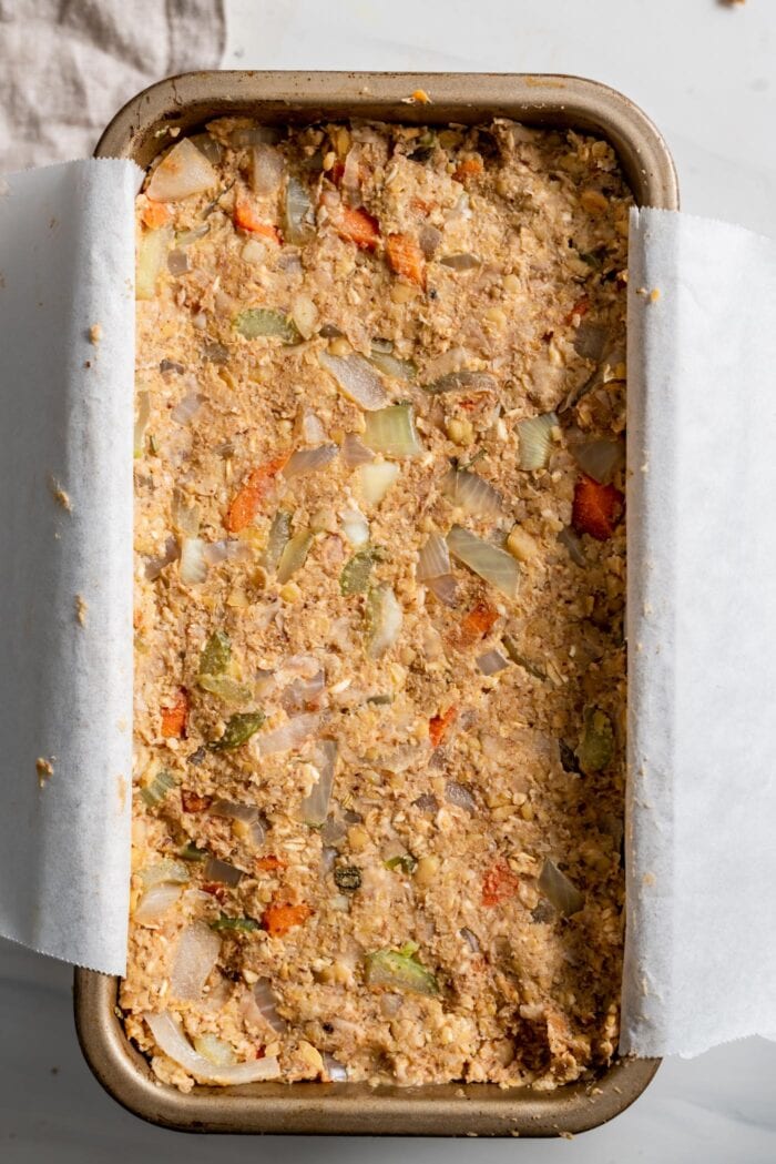 Raw chickpea loaf in a loaf pan lined with parchment paper.