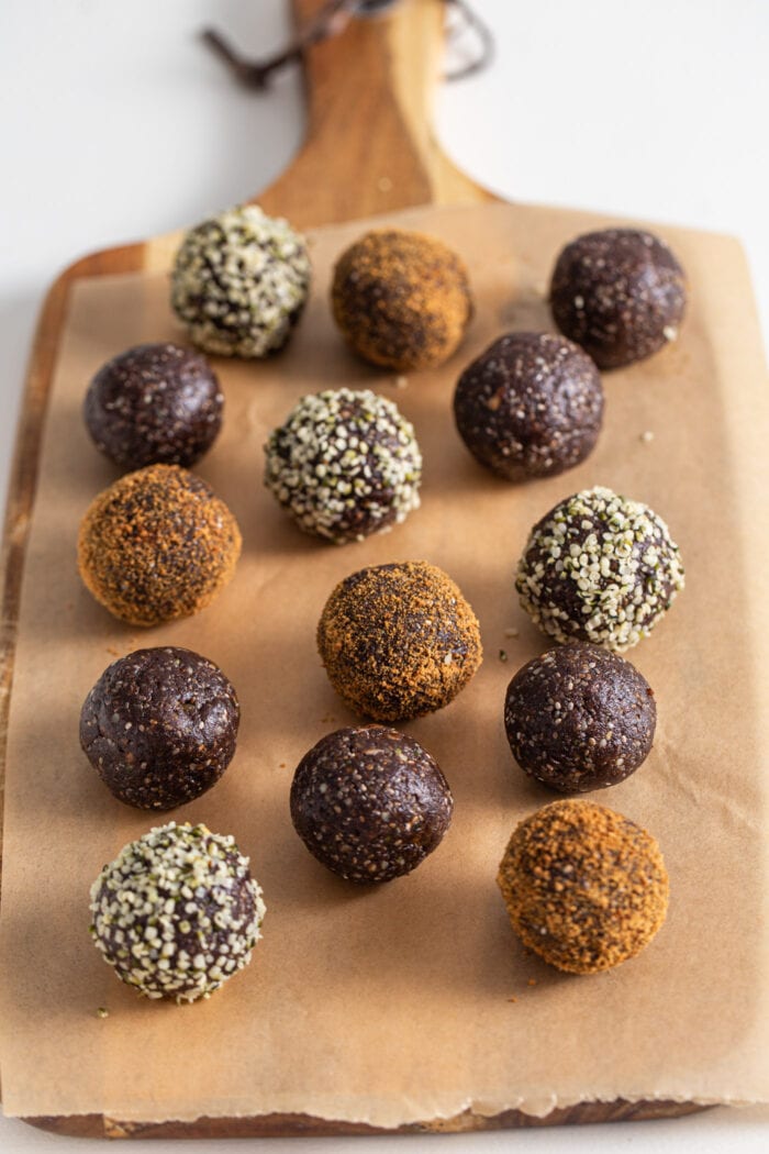 Chocolate energy balls rolled in coconut sugar and hemp seeds on a cutting board lined with parchment paper. The balls are made from dates, walnuts, cocoa and chia seeds.