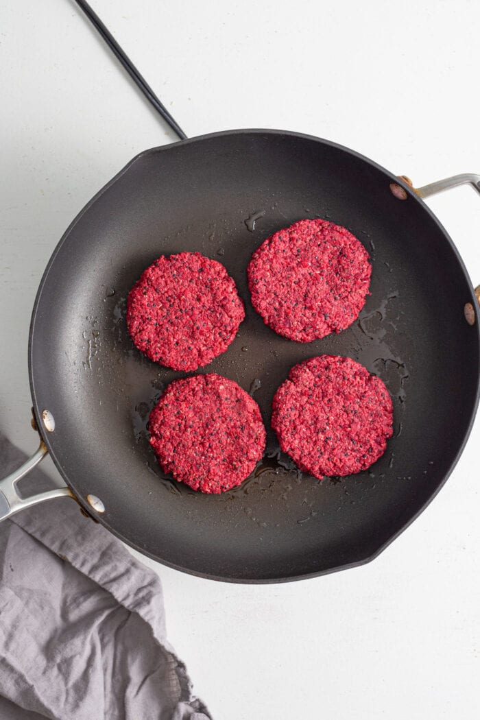 4 beet burgers cooking in a skiillet.