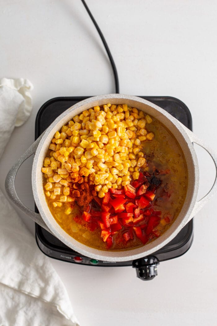 Corn and red bell peppers cooking in broth in a soup pot.
