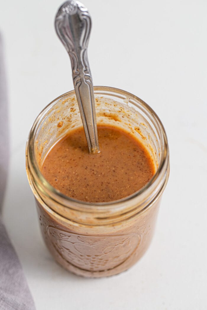 Creamy coconut almond butter sauce in a jar with a spoon resting in jar.