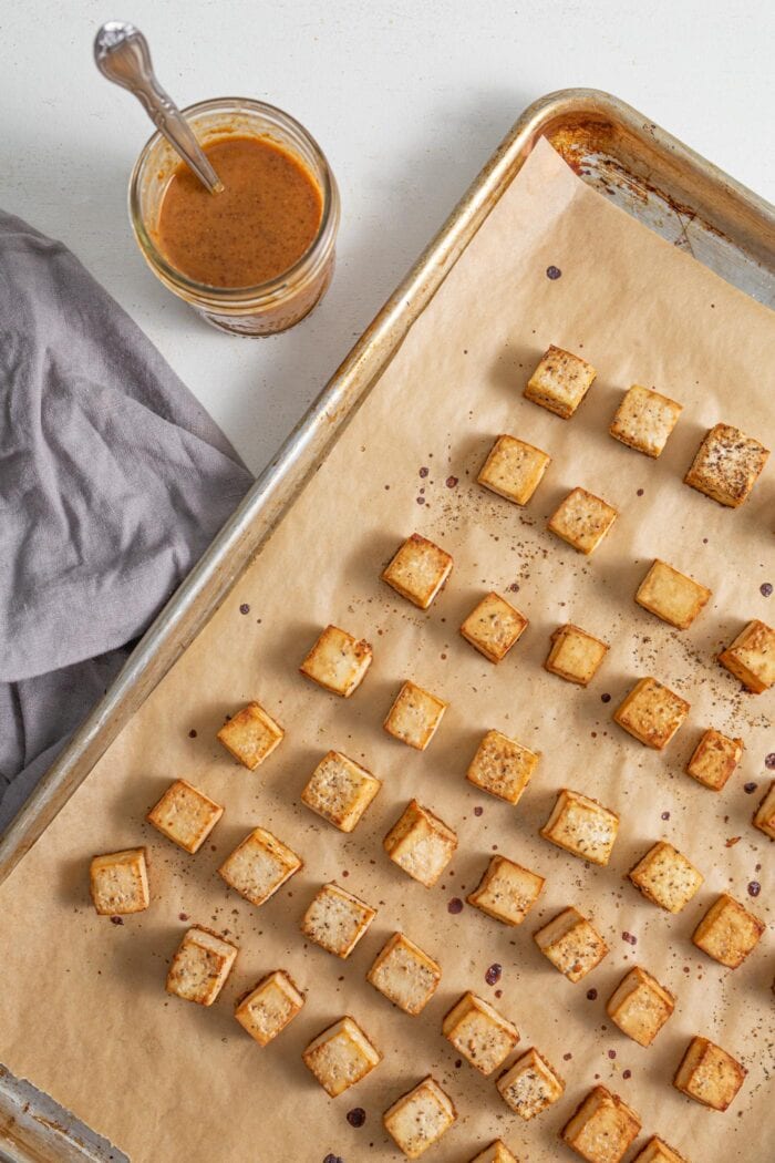 Cubed, baked tofu on a baking tray lined with parchment paper.