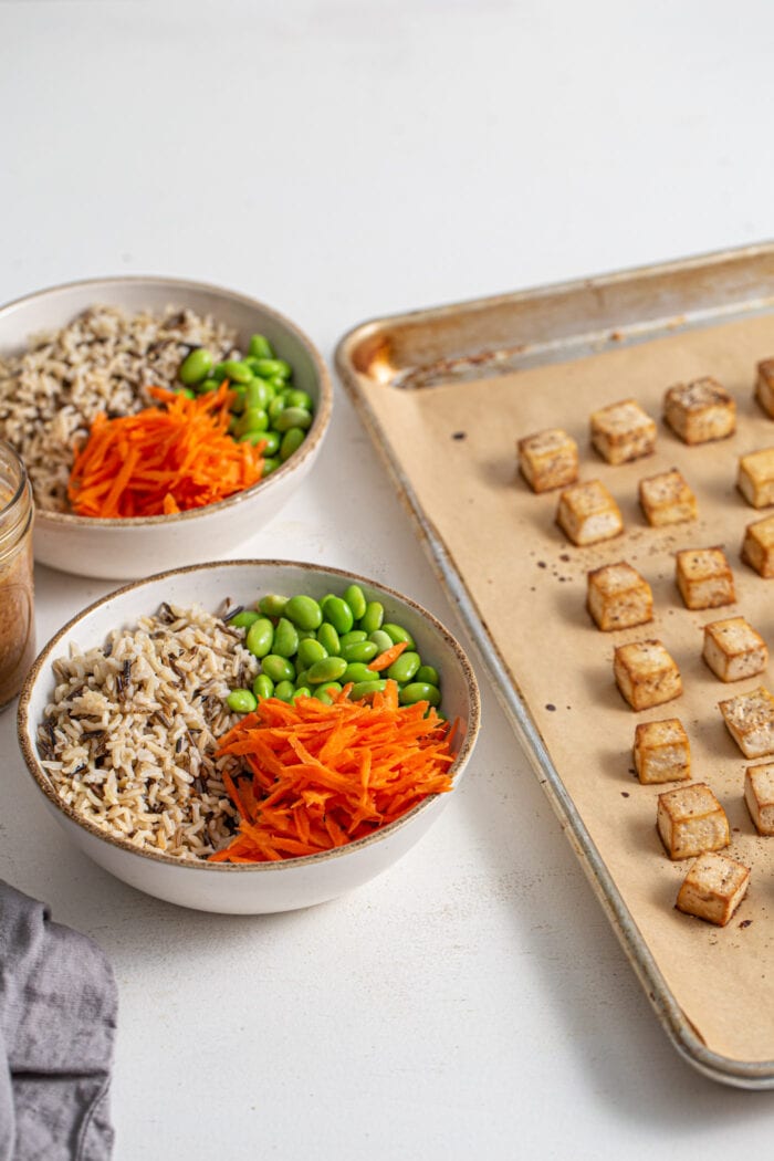 Bowl of rice, carrot and edamame sitting beside a baking tray of tofu.