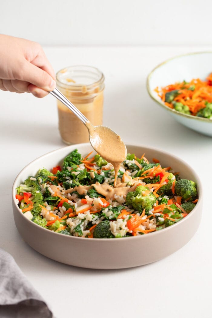Hand adding a spoonful of peanut sauce to a kale salad.