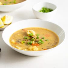 Bowl of vegan cauliflower wild rice soup topped with sliced green onion.