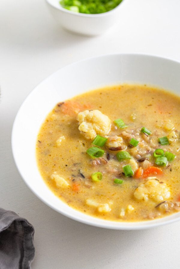 Bowl of cauliflower, carrot and wild rice soup topped with a few sliced green onions.